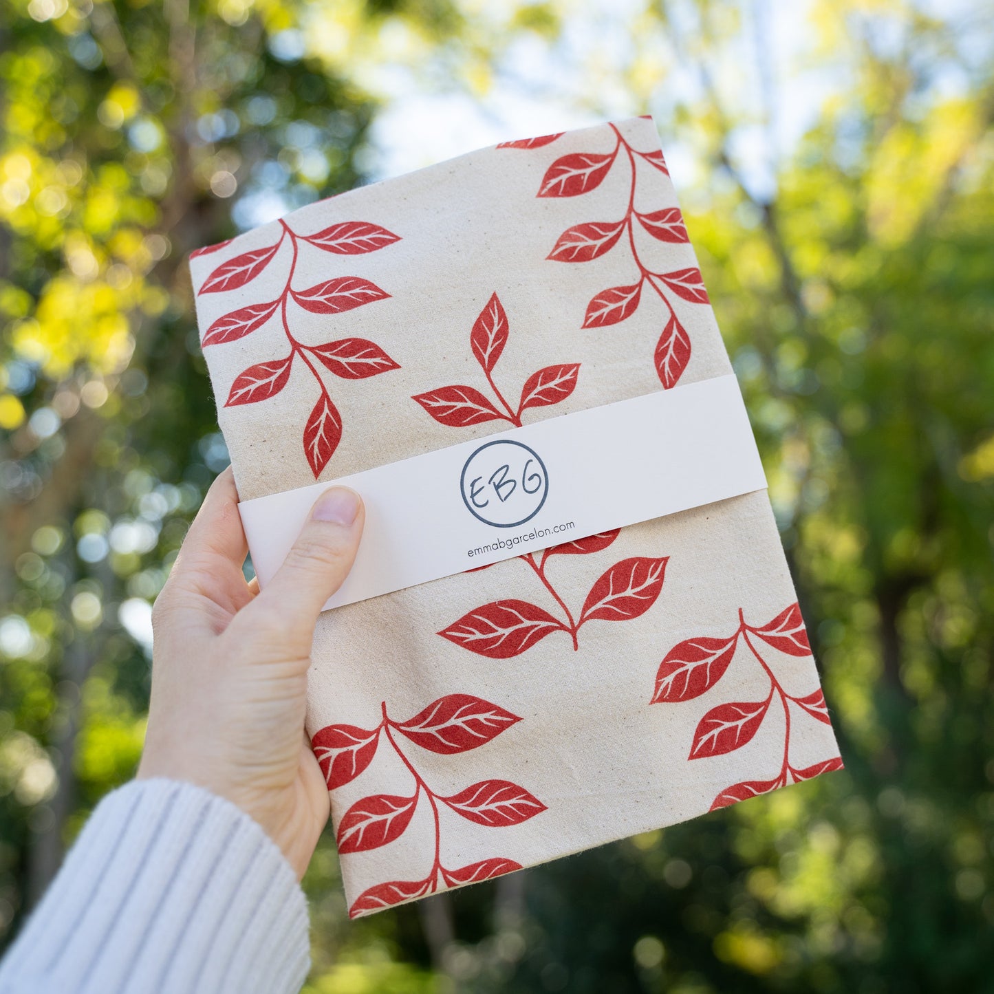 Hand holding a red botanical leaf tea towel outside