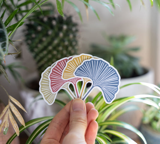 Hand holding four ginkgo leaf stickers in front of potted plants