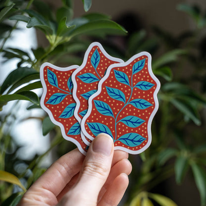 Hand holding 3 leaf stickers in turquoise, red, blue, and gold