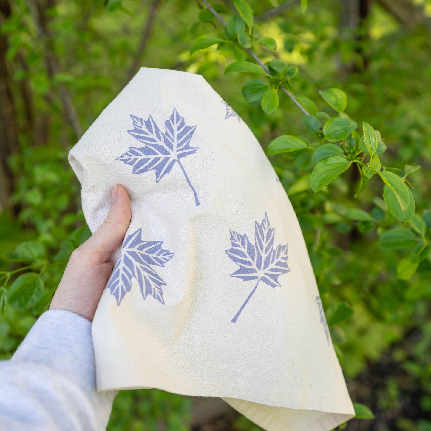 Hand holding a lavender maple leaf tea towel outside