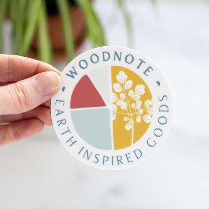 Hand holding a round Woodnote logo sticker