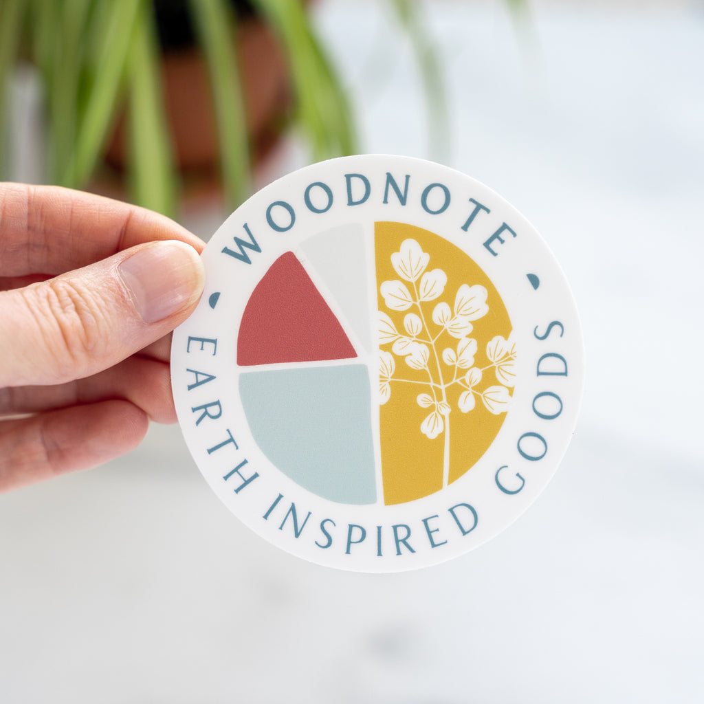 Hand holding a round Woodnote logo sticker