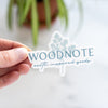 Hand holding a blue Woodnote logo sticker